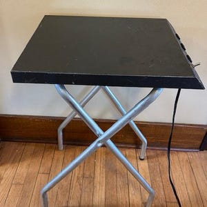 May include: A white ceramic mug with a black handle and the text "But First, Coffee" in a bold, black font. The mug is set against a blurred background, suggesting a cozy setting.