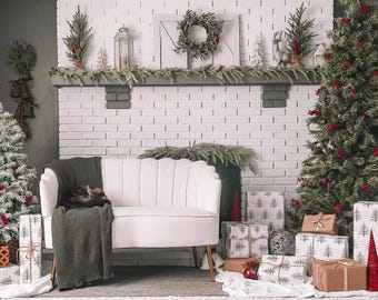 May include: A white tufted sofa with a green throw blanket and a cat sleeping on it. The sofa is in front of a white brick fireplace with a Christmas wreath and greenery above it. There are two Christmas trees on either side of the fireplace, decorated with red berries and ornaments.