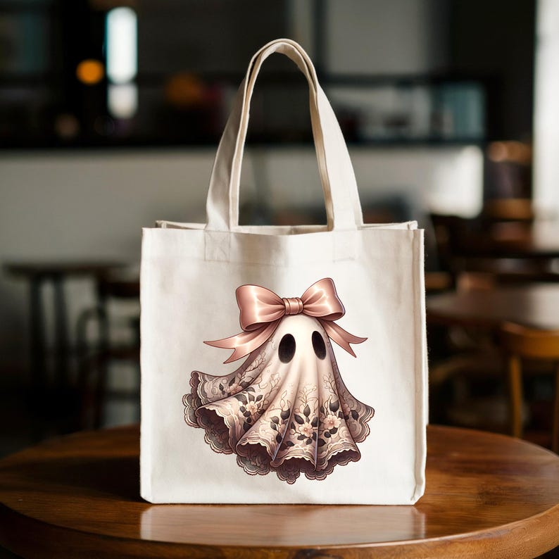 May include: A white canvas tote bag featuring a whimsical ghost design. The ghost is adorned with a pink bow and a delicate lace-like fabric with floral accents. The bag has sturdy handles and is set against a blurred background.