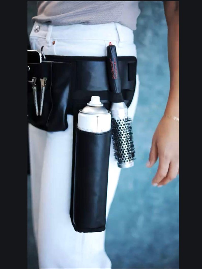 May include: A black leather hairstylist belt with a white hairspray can, a black and red hair styling tool, and a silver round brush.