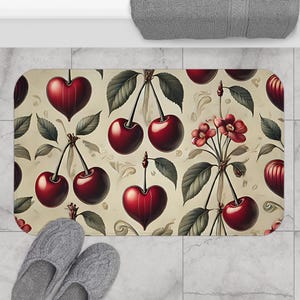 Può includere: Un tappetino da bagno color crema con un motivo ripetuto di ciliegie rosse, foglie verdi e fiori rossi. Le ciliegie sono rappresentate in uno stile realistico con una finitura lucida.