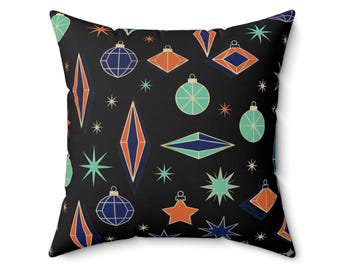 May include: A square throw pillow with a black background featuring a repeating pattern of mid-century style Christmas ornaments in shades of teal, navy blue, and orange, interspersed with various starburst shapes in light blue and white.