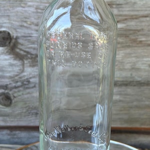 May include: Clear glass bottle with a metal cap. The bottle has embossed text that reads "FEDERAL LAW FORBIDS SALE OR RE-USE OF THIS BOTTLE" and "John Walker & Sons". The bottle is 1/5 quart.