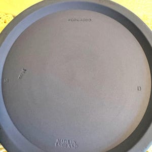 May include: A close-up of a light blue plate with the text "WEDGWOOD" and "MADE IN ENGLAND" embossed on the surface. The plate has a raised rim and a smooth, matte finish. The number "69" and the letter "D" are also visible.