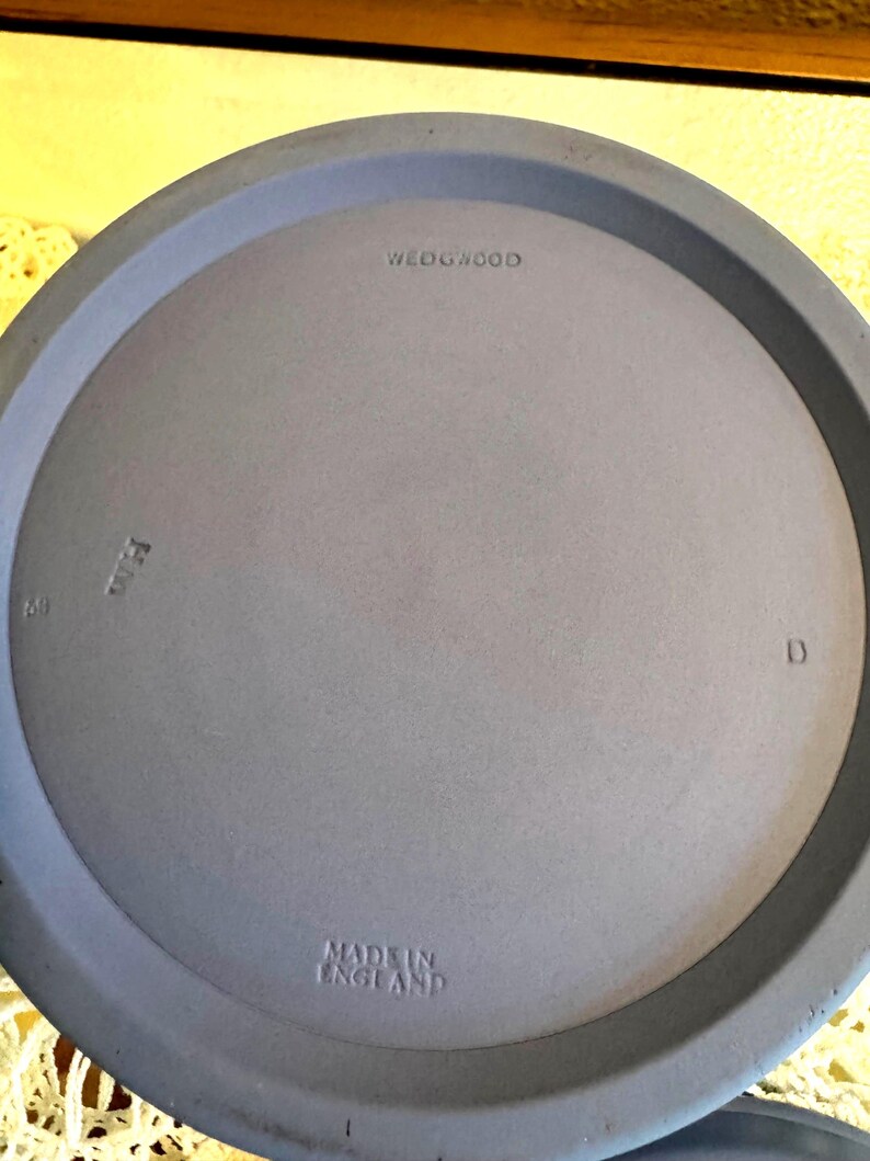 May include: A close-up of a light blue plate with the text "WEDGWOOD" and "MADE IN ENGLAND" embossed on the surface. The plate has a raised rim and a smooth, matte finish. The number "69" and the letter "D" are also visible.