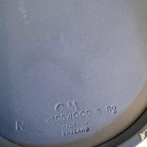 May include: Close-up of a blue Wedgwood ceramic piece. The text "CM WEDGWOOD &copy; 82 MADE IN ENGLAND" is stamped on the surface. The letter "N" is also visible. The piece has a matte finish.