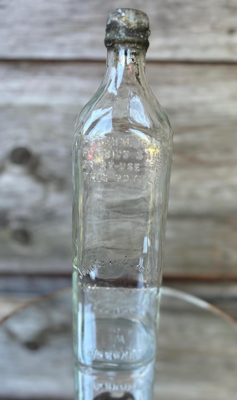 May include: Clear glass bottle with a metal cap. The bottle has embossed text that reads "Federal Law Forbids Sale or Re-Use of This Bottle." The bottle is rectangular with rounded shoulders.