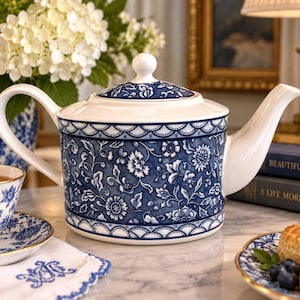 May include: A white ceramic teapot featuring a deep blue floral pattern and a scalloped border design. The teapot has a curved handle, a tapered spout, and a matching lid with a round knob, showcasing a classic blue and white color scheme.