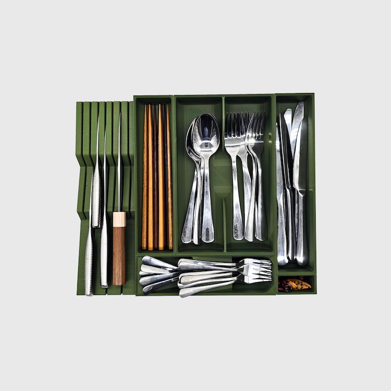 Puede incluir: Un organizador de cubiertos verde lleno de cubiertos de acero inoxidable, que incluye cuchillos, tenedores, cucharas y palillos. El organizador tiene m&uacute;ltiples compartimentos para mantener los utensilios ordenados. Los utensilios est&aacute;n ordenados.