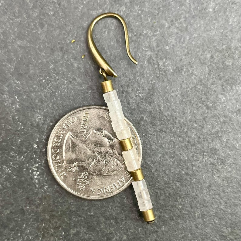 May include: A gold earring with a white stone dangle. The dangle is made of multiple square-shaped stones with gold spacers between each stone.
