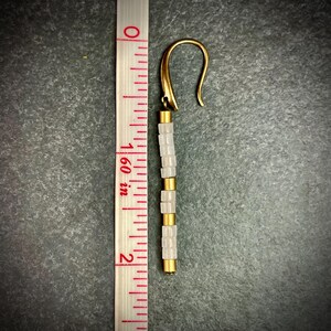 May include: A pair of gold tone earrings with white beads. The earrings are approximately 2 inches long.