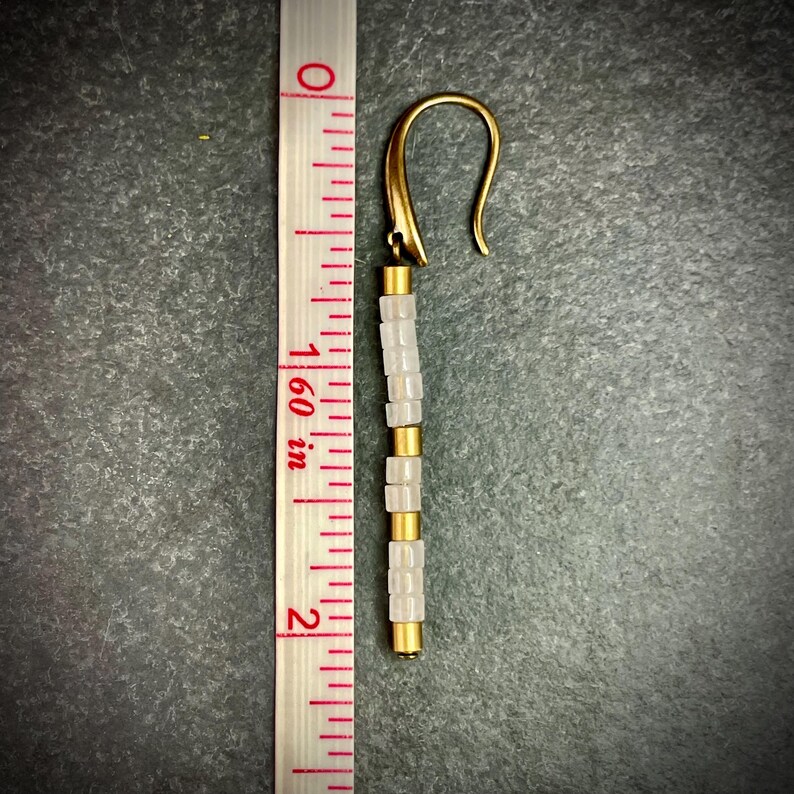 May include: A pair of gold tone earrings with white beads. The earrings are approximately 2 inches long.