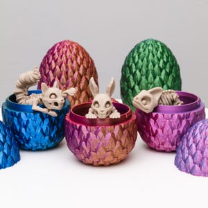 May include: Five dragon egg-shaped containers with a metallic finish in blue, green, pink, and purple. Each container has a small, detailed, white skeletal creature inside.