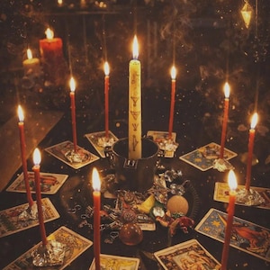 May include: A dimly lit scene featuring lit candles arranged around tarot cards and various mystical objects. A central, taller candle stands in a metal container, surrounded by smaller red candles. The overall aesthetic suggests a spiritual or occult theme.