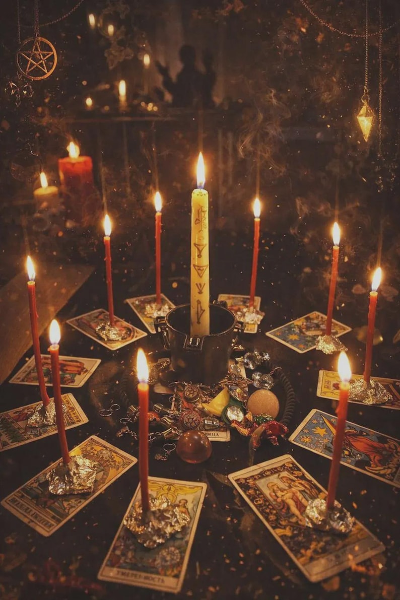 May include: A dimly lit scene featuring lit candles arranged around tarot cards and various mystical objects. A central, taller candle stands in a metal container, surrounded by smaller red candles. The overall aesthetic suggests a spiritual or occult theme.