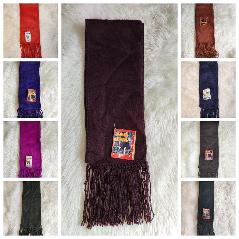 May include: A collection of colorful alpaca wool scarves with fringe. The scarves are in various colors, including red, purple, blue, and brown. Each scarf has a tag with an image of an alpaca.