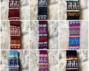 May include: Nine colorful knitted leg warmers with various patterns and designs. Each leg warmer features a unique combination of colors, including red, blue, purple, and yellow, with geometric and animal motifs. The leg warmers are displayed on a white, fluffy surface.