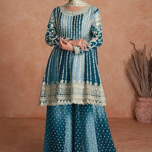 May include: A teal and light blue embroidered salwar kameez set. The long-sleeved top features vertical stripes and ornate gold embroidery along the neckline, sleeves, and hem. The matching palazzo pants have a dotted pattern and gold trim.