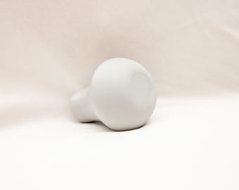 May include: A white ceramic vase with a rounded shape and a wide opening. The vase is sitting on a white surface.