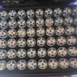 May include: A white ceramic mug with a black handle and the text "But First, Coffee" in a bold, black font. The mug is filled with a dark liquid, likely coffee, and sits on a light-colored surface.