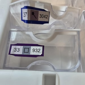 May include: Two clear plastic storage containers stacked on top of each other. Each container has a label with numbers and a symbol. The top label reads "37" and "3042". The bottom label reads "33" and "932".