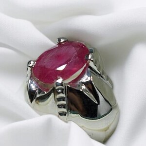 K&ouml;nnte beinhalten: Ein silberner Ring mit einem gro&szlig;en, ovalen Rubin-Edelstein. Der Ring hat eine detaillierte, strukturierte Band.