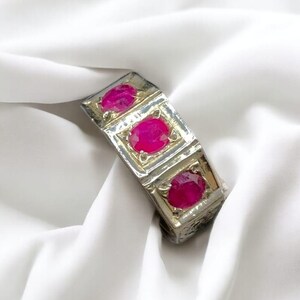 Op de afbeelding: Een zilveren ring met drie roze ovale edelstenen gezet in vierkante frames.