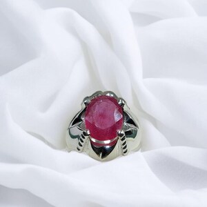 K&ouml;nnte beinhalten: Ein silberner Ring mit einem gro&szlig;en, ovalen, roten Edelstein, der in einer Krappenfassung sitzt.