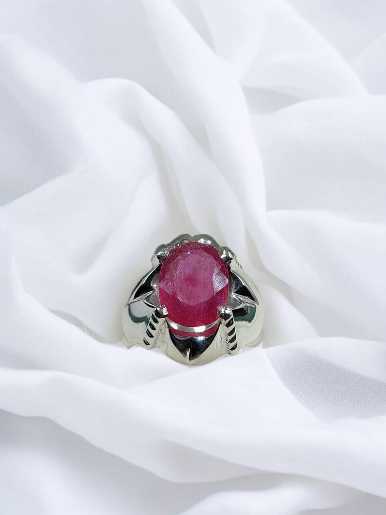 K&ouml;nnte beinhalten: Ein silberner Ring mit einem gro&szlig;en, ovalen, roten Edelstein, der in einer Krappenfassung sitzt.