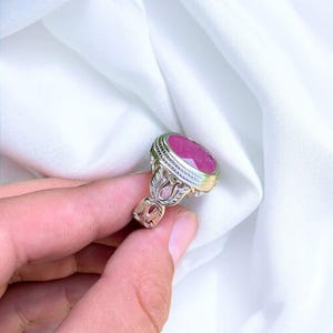 Op de afbeelding: Een zilveren ring met een sierlijk ontwerp en een grote, ovale robijn.