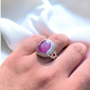 Op de afbeelding: Een zilveren ring met een grote, ovale, roze edelsteen gezet in een decoratieve zilveren setting.