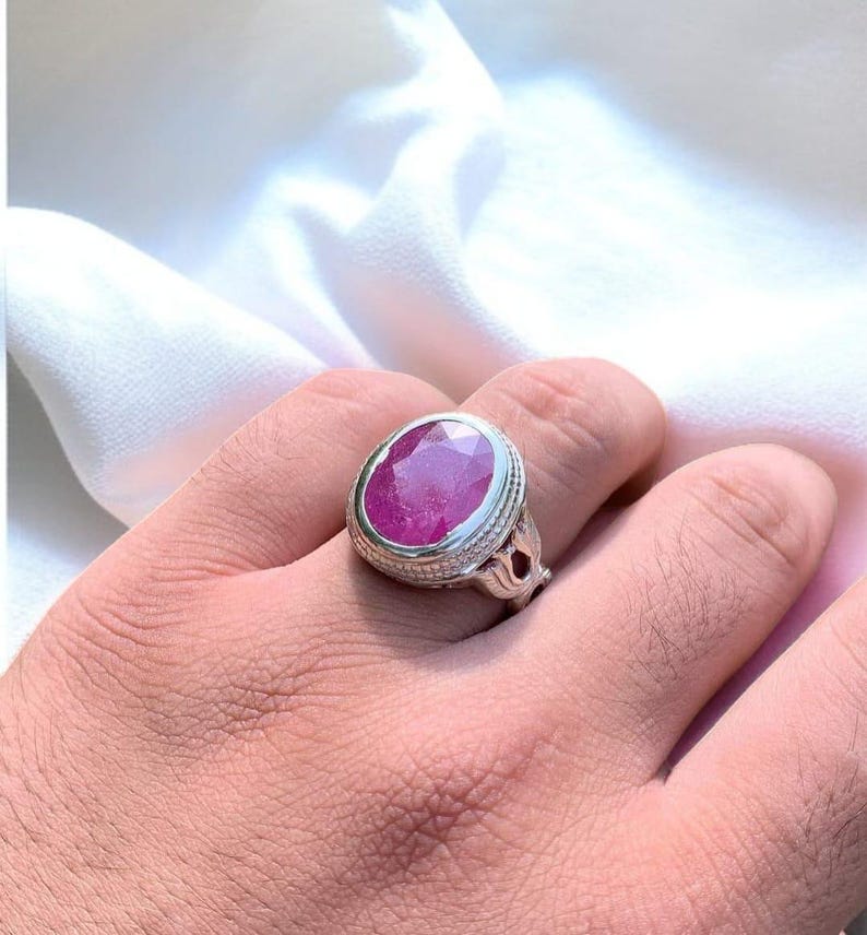 Op de afbeelding: Een zilveren ring met een grote, ovale, roze edelsteen gezet in een decoratieve zilveren setting.