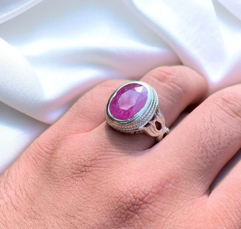 Op de afbeelding: Een zilveren ring met een grote, ovale, roze robijn die is gezet in een decoratieve zilveren band.