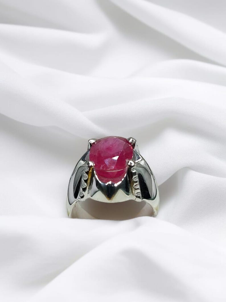 K&ouml;nnte beinhalten: Ein silberner Ring mit einem gro&szlig;en, ovalen Rubin-Edelstein. Der Rubin ist tiefrot und hat einen facettierten Schliff.