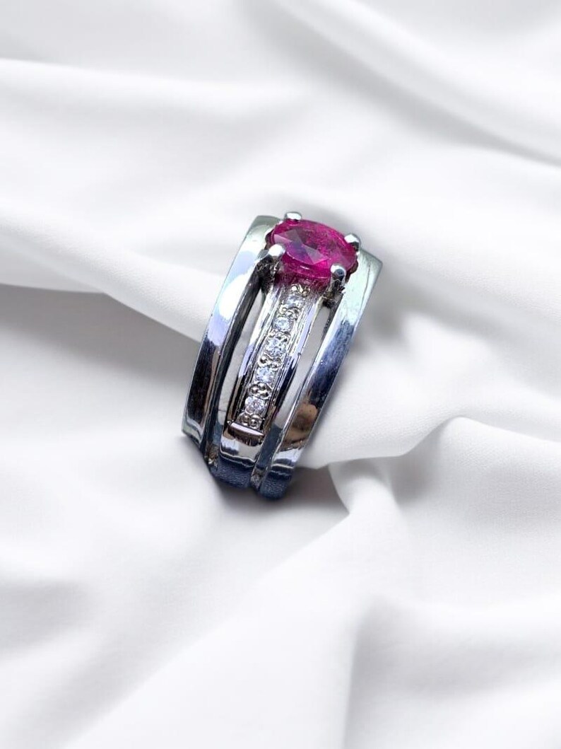 K&ouml;nnte beinhalten: Ein silberner Ring mit einem rosafarbenen ovalen Edelstein und einer Reihe kleiner, klarer Edelsteine.