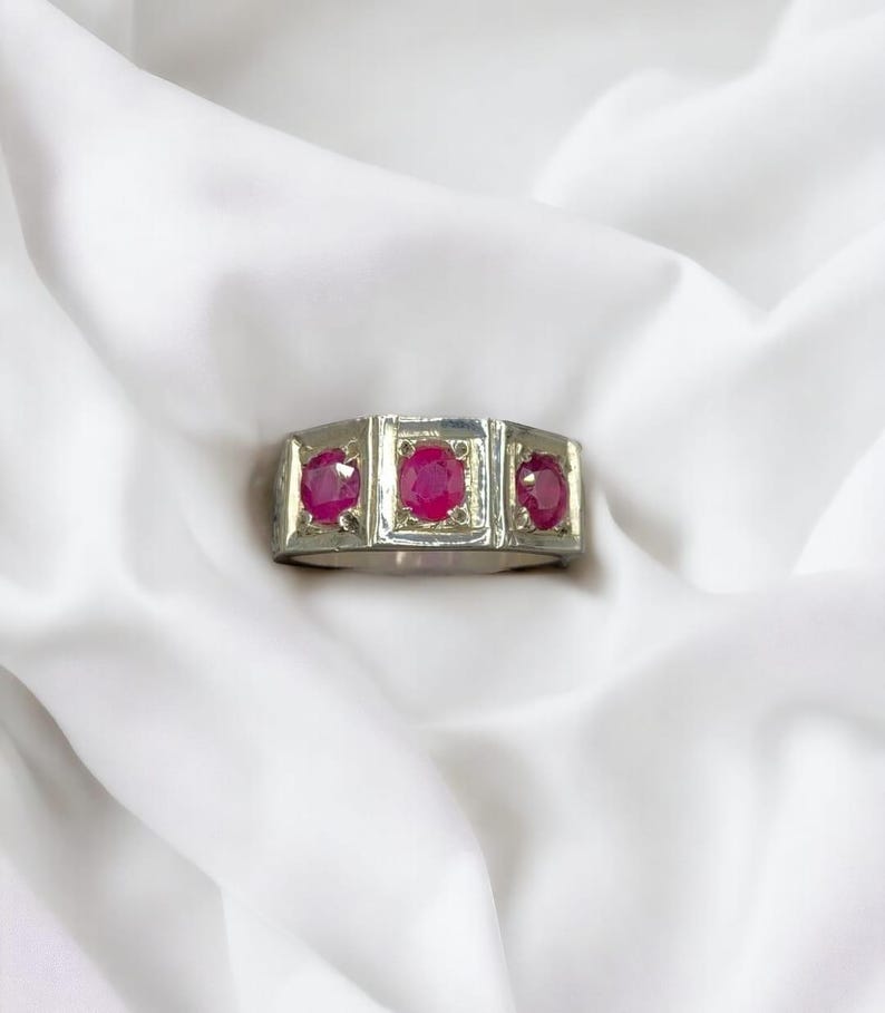 Op de afbeelding: Een zilveren ring met drie rode robijnstenen die in een vierkante vorm zijn gezet.