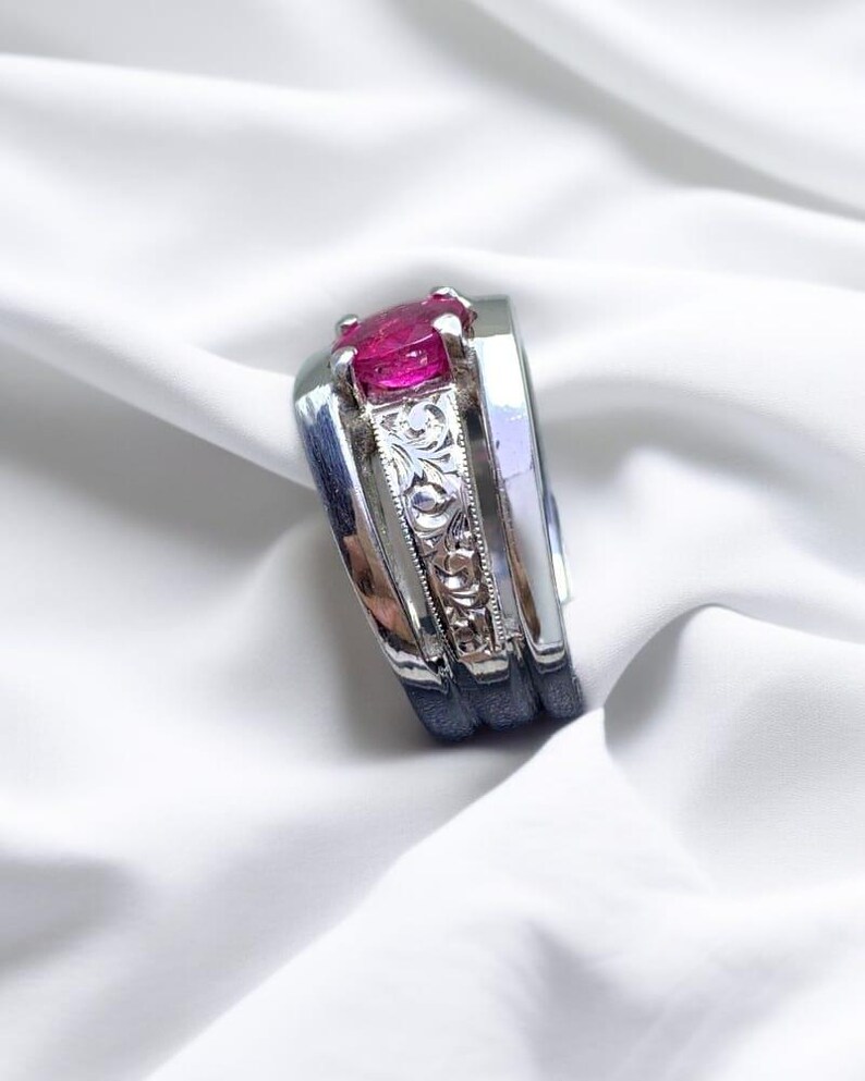 K&ouml;nnte beinhalten: Ein silberner Ring mit einem rosafarbenen Edelstein in der Mitte. Die Band ist mit einem floralen Muster graviert.