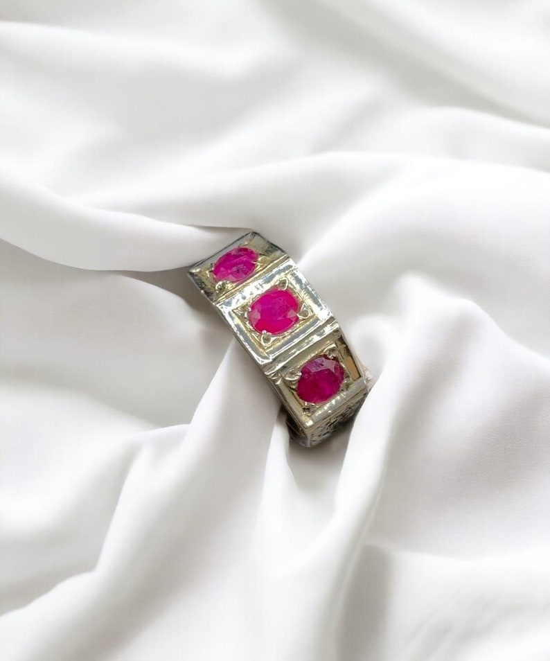 Op de afbeelding: Een zilveren ring met drie roze ovale edelstenen gezet in vierkante frames.
