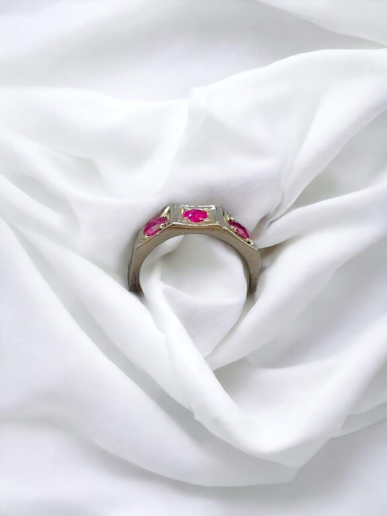 Op de afbeelding: Een gouden ring met vier rode edelstenen die in een vierkante vorm zijn gezet. De ring ligt op een witte stoffen achtergrond.