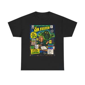 May include: A black t-shirt featuring a comic book cover graphic titled The QA Tester. The illustration depicts a person at a computer desk with a large green monster looming behind, surrounded by stacks of papers, a mug, and various text elements.