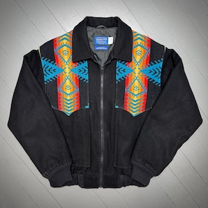May include: Black zip-up jacket with colorful geometric patterns on the chest and shoulders. The jacket features a collar, two front pockets, and ribbed cuffs. The Pendleton label is visible on the inside of the jacket.