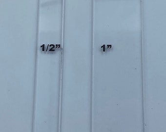Puede incluir: Una plantilla de plástico transparente con medidas marcadas en pulgadas. La plantilla tiene una abertura rectangular con dimensiones de 1 pulgada por 5/8 pulgada. La plantilla es útil para manualidades y proyectos de bricolaje.