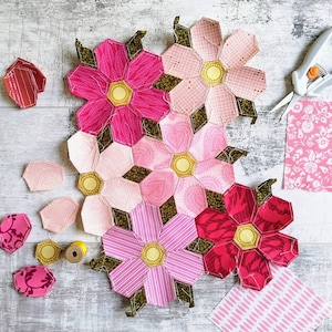 Könnte beinhalten: Nahaufnahme eines rosa-grünen Stoffblumen-Quiltblocks. Der Block besteht aus mehreren einzelnen Blumenformen, jede mit einem anderen Muster. Die Blumen sind zusammengenäht, um ein größeres Design zu schaffen.