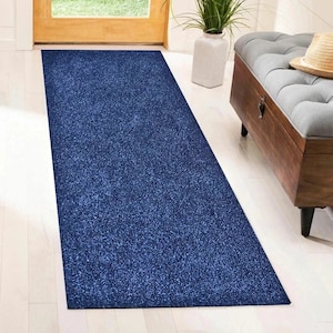 May include: A long, rectangular, navy blue rug with a textured surface. The rug is placed in a hallway, leading towards a wooden door. The rug's color is a deep, solid blue, providing a contrast to the light-coloured flooring.