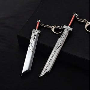 May include: Two silver sword keychains with red accents. The swords are detailed with intricate designs and have a sharp point. The keychains are attached to a silver chain.