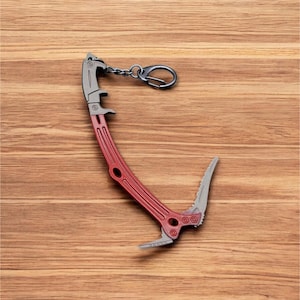 May include: A red and silver metal keychain shaped like a climbing ice axe. The keychain has a bottle opener and a key ring.