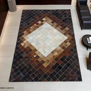 May include: A rectangular rug with a diamond pattern. The rug has a central diamond of off-white squares, surrounded by concentric diamond shapes in shades of brown and black. The rug is made of a material that appears to be leather or hide. The rug has the text "MBM CARPETS".