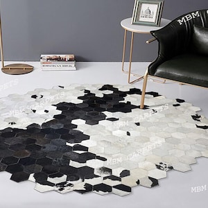 Puede incluir: Una alfombra circular compuesta por numerosos parches hexagonales pequeños en negro, blanco y gris. Los parches están dispuestos para crear un patrón abstracto a gran escala en la superficie de la alfombra, con un aspecto texturizado.