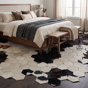 Könnte beinhalten: Ein großer Teppich aus einzelnen sechseckigen Fliesen aus Rindsleder in einem Patchwork-Muster aus Schwarz-, Weiß- und Brauntönen. Der Teppich weist ein sich wiederholendes geometrisches Design auf, das den Boden unter einem Holzbett und einer Bank bedeckt.