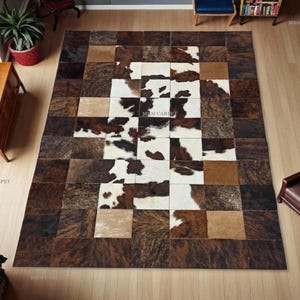 May include: A large rectangular cowhide rug with a patchwork design. The rug features squares of brown, tan, and white with brown spots. The rug is a decorative floor covering.